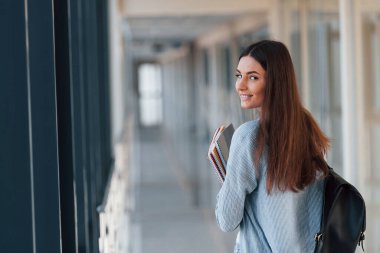 Bir üniversitenin koridorunda elinde not defterleri olan genç bir kız öğrencinin arka görüntüsü..