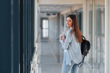 Bir üniversitenin koridorunda elinde not defterleri olan genç bir kız öğrencinin arka görüntüsü..