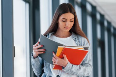 Üniversite koridorunda not defterinden bilgi okuyan genç bir kız öğrenci..