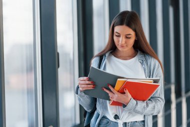 Üniversite koridorunda not defterinden bilgi okuyan genç bir kız öğrenci..