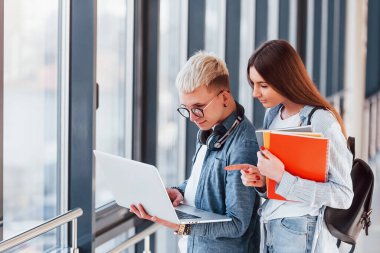 İki genç öğrenci, üniversitenin koridorunda dizüstü bilgisayarlarıyla birlikte..