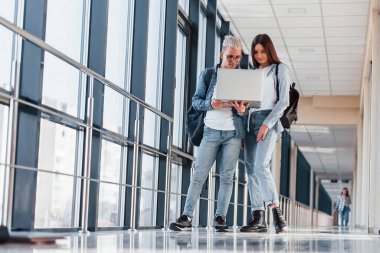 İki genç öğrenci, üniversitenin koridorunda dizüstü bilgisayarlarıyla birlikte..