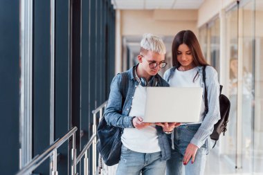 İki genç öğrenci, üniversitenin koridorunda dizüstü bilgisayarlarıyla birlikte..