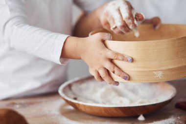 Close up view of woman with her granddaughter preparing food with flour on kitchen.