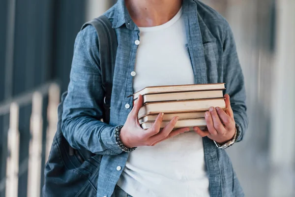 Kolejin koridorunda elinde kitaplarla gezen kot elbiseli genç bir öğrenciyi yakından izleyin..