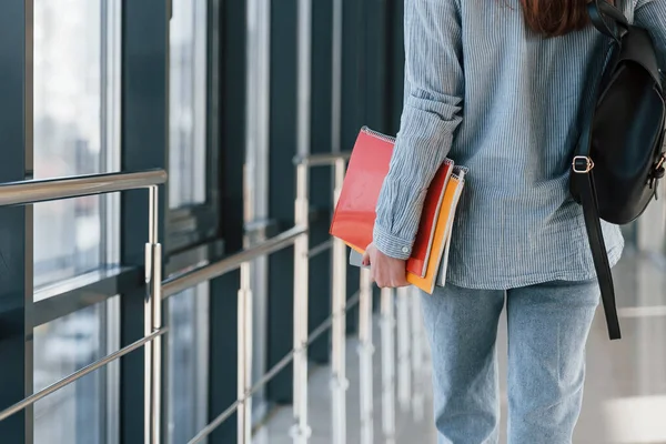 Bir üniversitenin koridorunda elinde not defterleri olan genç kız öğrenciye yakından bakın..