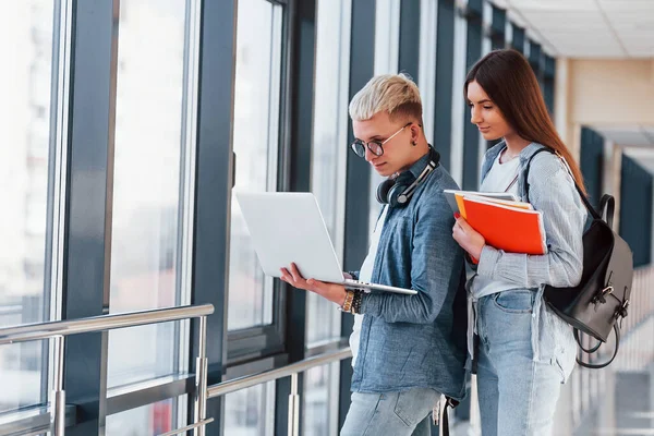İki genç öğrenci, üniversitenin koridorunda dizüstü bilgisayarlarıyla birlikte..