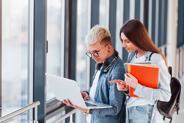İki genç öğrenci, üniversitenin koridorunda dizüstü bilgisayarlarıyla birlikte..