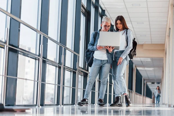 İki genç öğrenci, üniversitenin koridorunda dizüstü bilgisayarlarıyla birlikte..