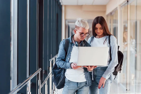 İki genç öğrenci, üniversitenin koridorunda dizüstü bilgisayarlarıyla birlikte..