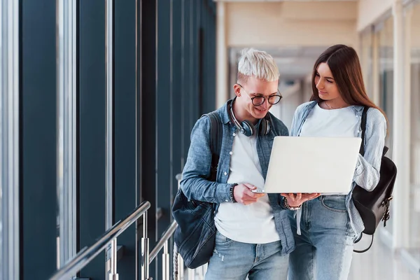 İki genç öğrenci, üniversitenin koridorunda dizüstü bilgisayarlarıyla birlikte..