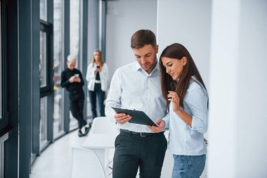 Kadın ve erkek, ofiste birlikte çalışan ve iletişim kuran başarılı genç takımın önünde belgeler hakkında konuşuyorlar..