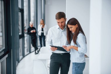 Kadın ve erkek, ofiste birlikte çalışan ve iletişim kuran başarılı genç takımın önünde belgeler hakkında konuşuyorlar..
