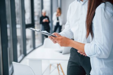 Kadın ve erkek, ofiste birlikte çalışan ve iletişim kuran başarılı genç takımın önünde belgeler hakkında konuşuyorlar..