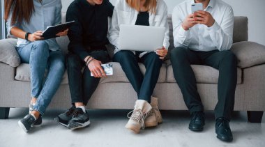 Group of friends sitting on the sofa with laptop and phones together.