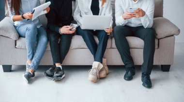 Group of friends sitting on the sofa with laptop and phones together.