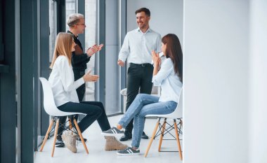 Bir grup başarılı genç takım, pencere kenarındaki ofiste birlikte çalışıyor ve iletişim kuruyor..