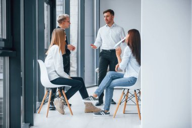 Bir grup başarılı genç takım, pencere kenarındaki ofiste birlikte çalışıyor ve iletişim kuruyor..