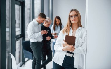 Ofiste birlikte çalışan ve iletişim kuran başarılı genç takımın önünde duran notlu neşeli sarışının portresi..