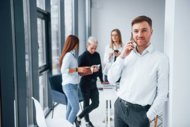 Resmi kıyafetli bir adam portresi ve ofiste birlikte çalışan ve iletişim kuran başarılı genç bir takımın önünde duran bir telefon..