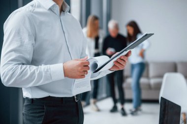 Resmi kıyafetli bir adam, ofiste birlikte çalışan ve iletişim kuran genç ve başarılı bir ekibin önünde duruyor..