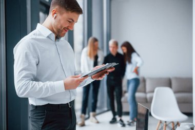 Resmi kıyafetli bir adam, ofiste birlikte çalışan ve iletişim kuran genç ve başarılı bir ekibin önünde duruyor..