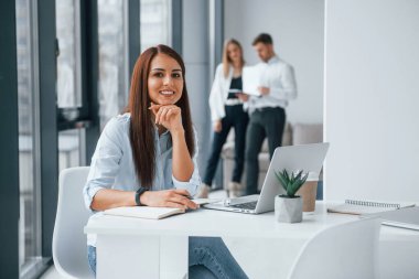 Dizüstü bilgisayarı olan bir kadın ofiste birlikte çalışan ve iletişim kuran başarılı genç bir takım grubunun önünde oturuyor..