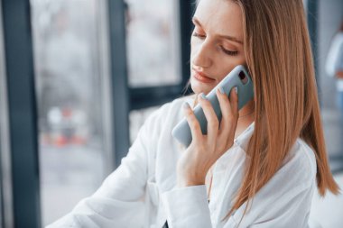 Resmi kıyafetli genç bir sarışın ofiste çalışıyor ve telefonla konuşuyor..
