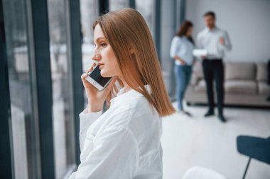 Ofiste birlikte çalışan ve iletişim kuran bir grup başarılı genç kızın önünde telefonla konuşan bir kadın..