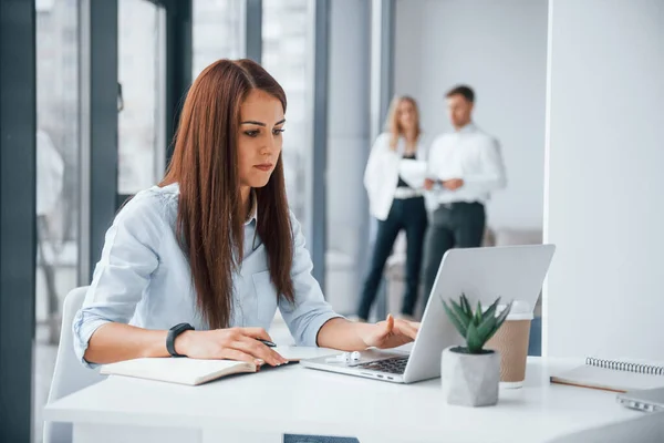 職場で屋内で一緒に働くと通信する若い成功したチームのグループの前に座っているラップトップを持つ女性 — ストック写真
