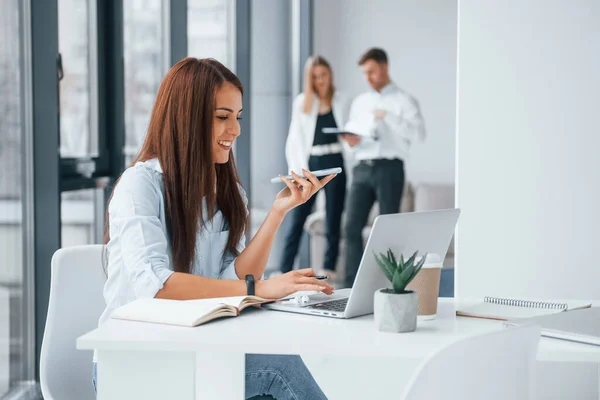 Woman with laptop sitting in front of group of young successful team that working and communicating together indoors in office.