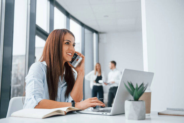 Женщина с ноутбуком сидит перед группой молодых успешной команды, которые работают и общаться вместе в помещении в офисе.