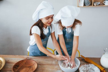 Mutfakta un taşıyan mavi şef üniformalı iki küçük kız..