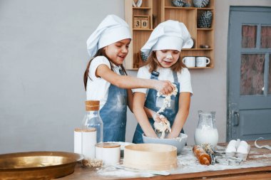 Mavi şef üniformalı iki küçük kız mutfakta yemek hazırlıyor..