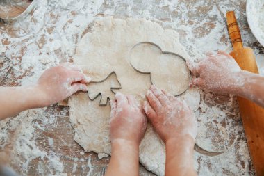 Masadaki aletle yoğurmaya hazırlanan iki küçük kızın ellerinin üst görüntüsü.