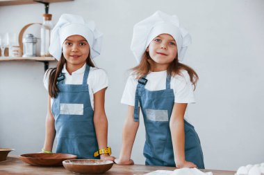 Mavi şef üniformalı iki küçük kız mutfakta yemek hazırlıyor..