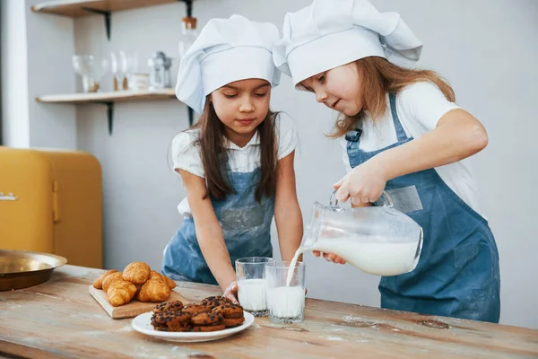 Two Little Girls Blue Chef Uniform Pouring Milk Glasses Kitchen — стоковое фото