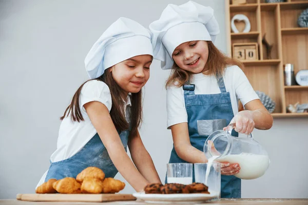 Two Little Girls Blue Chef Uniform Pouring Milk Glasses Kitchen — стоковое фото
