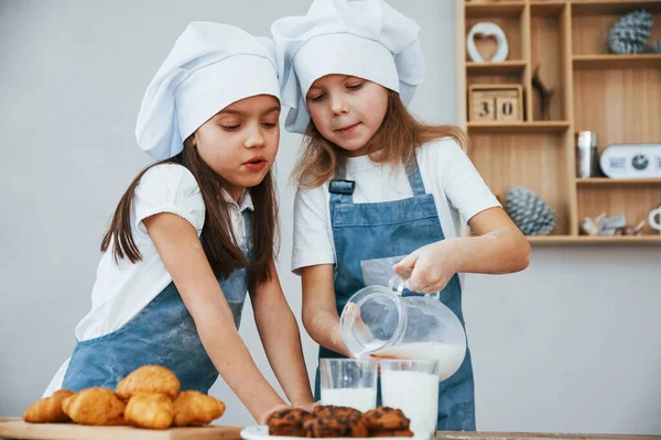 Two Little Girls Blue Chef Uniform Pouring Milk Glasses Kitchen — Stockfoto