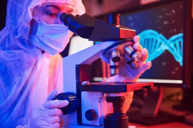 Maskeli hemşire ve beyaz üniformalı hemşire laboratuarda bilgisayar, mikroskop ve tıbbi ekipmanla Coronavirus aşısını arıyor..