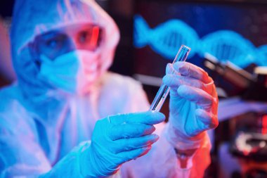 Maskeli hemşire ve beyaz üniformalı, elinde sıvı tüple neon ışıklı laboratuarda oturmuş Coronavirus aşısını arıyor..