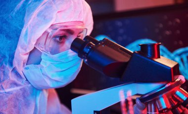 Maskeli hemşire ve beyaz üniformalı hemşire laboratuarda bilgisayar, mikroskop ve tıbbi ekipmanla Coronavirus aşısını arıyor..