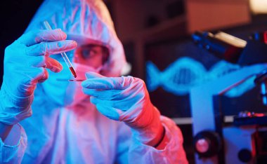 Maskeli hemşire ve beyaz üniformalı, elinde sıvı tüple neon ışıklı laboratuarda oturmuş Coronavirus aşısını arıyor..