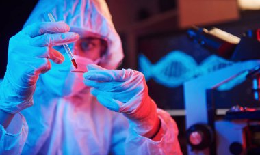 Maskeli hemşire ve beyaz üniformalı, elinde sıvı tüple neon ışıklı laboratuarda oturmuş Coronavirus aşısını arıyor..