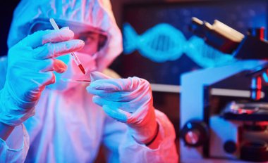 Maskeli hemşire ve beyaz üniformalı, elinde sıvı tüple neon ışıklı laboratuarda oturmuş Coronavirus aşısını arıyor..