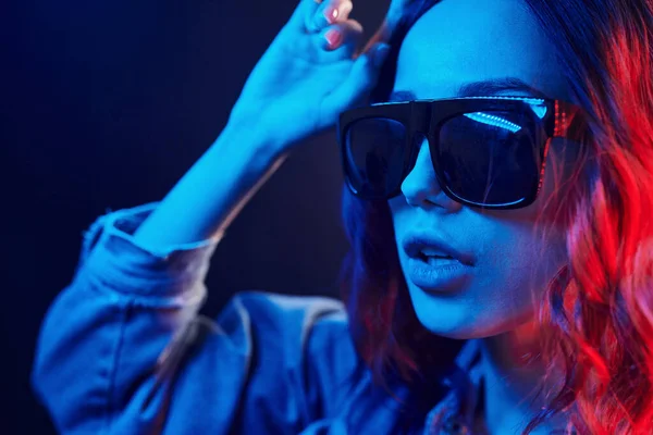 Portrait of young girl in sunglasses in red and blue neon in studio.