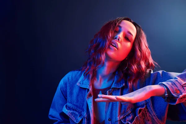 Portrait of young girl with curly hair that dancing in red and blue neon in studio.