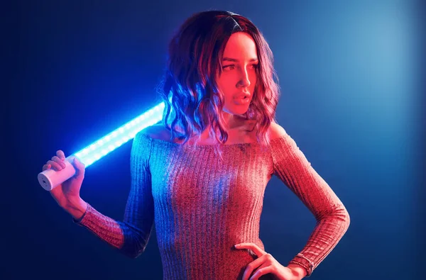 Portrait of young girl with curly hair that holds lighting sticks in red and blue neon in studio.