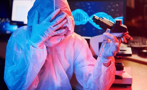 Maskeli hemşire ve beyaz üniformalı, elinde sıvı tüple neon ışıklı laboratuarda oturmuş Coronavirus aşısını arıyor..