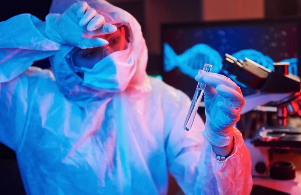 Maskeli hemşire ve beyaz üniformalı, elinde sıvı tüple neon ışıklı laboratuarda oturmuş Coronavirus aşısını arıyor..